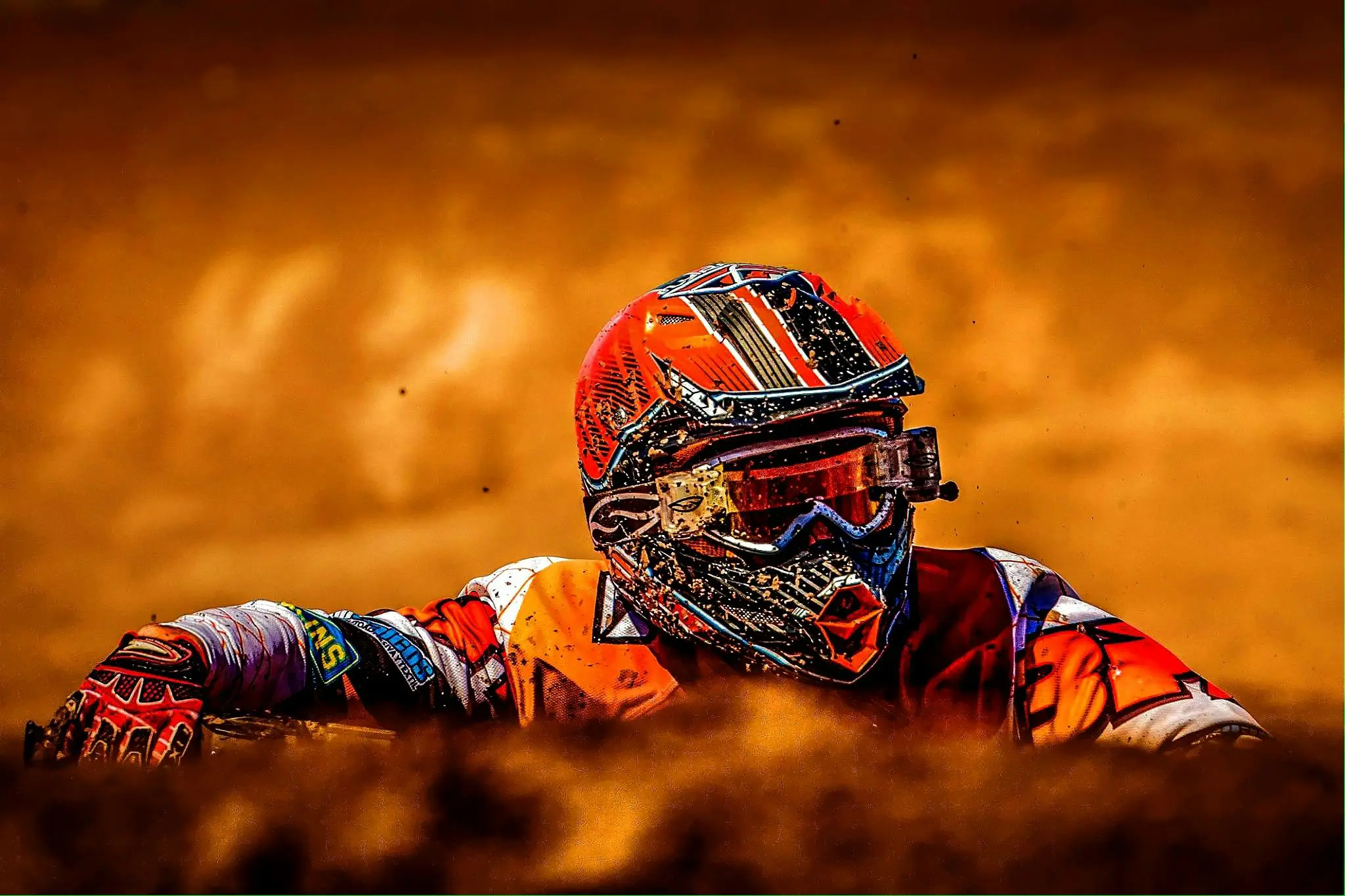 Motocross rider in vibrant gear amid dusty action.