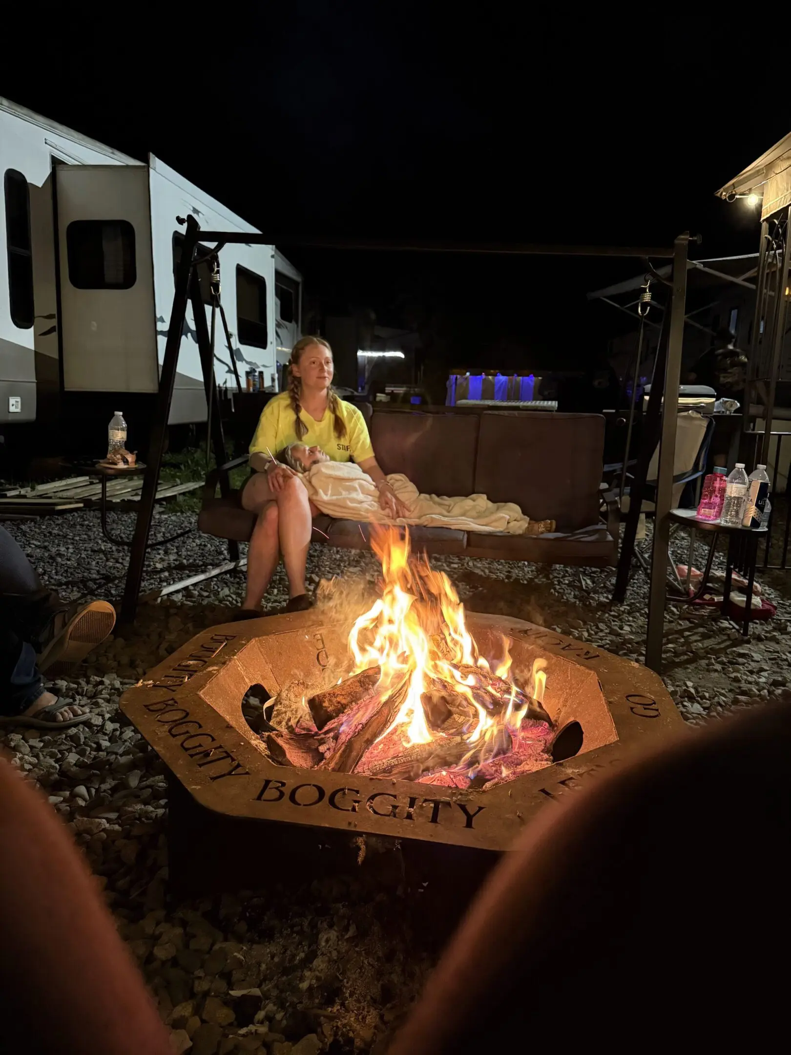 Person warming hands by a campfire at night near an RV.