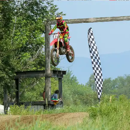 A motocross rider jumps over a wooden ramp with a checkered flag nearby.